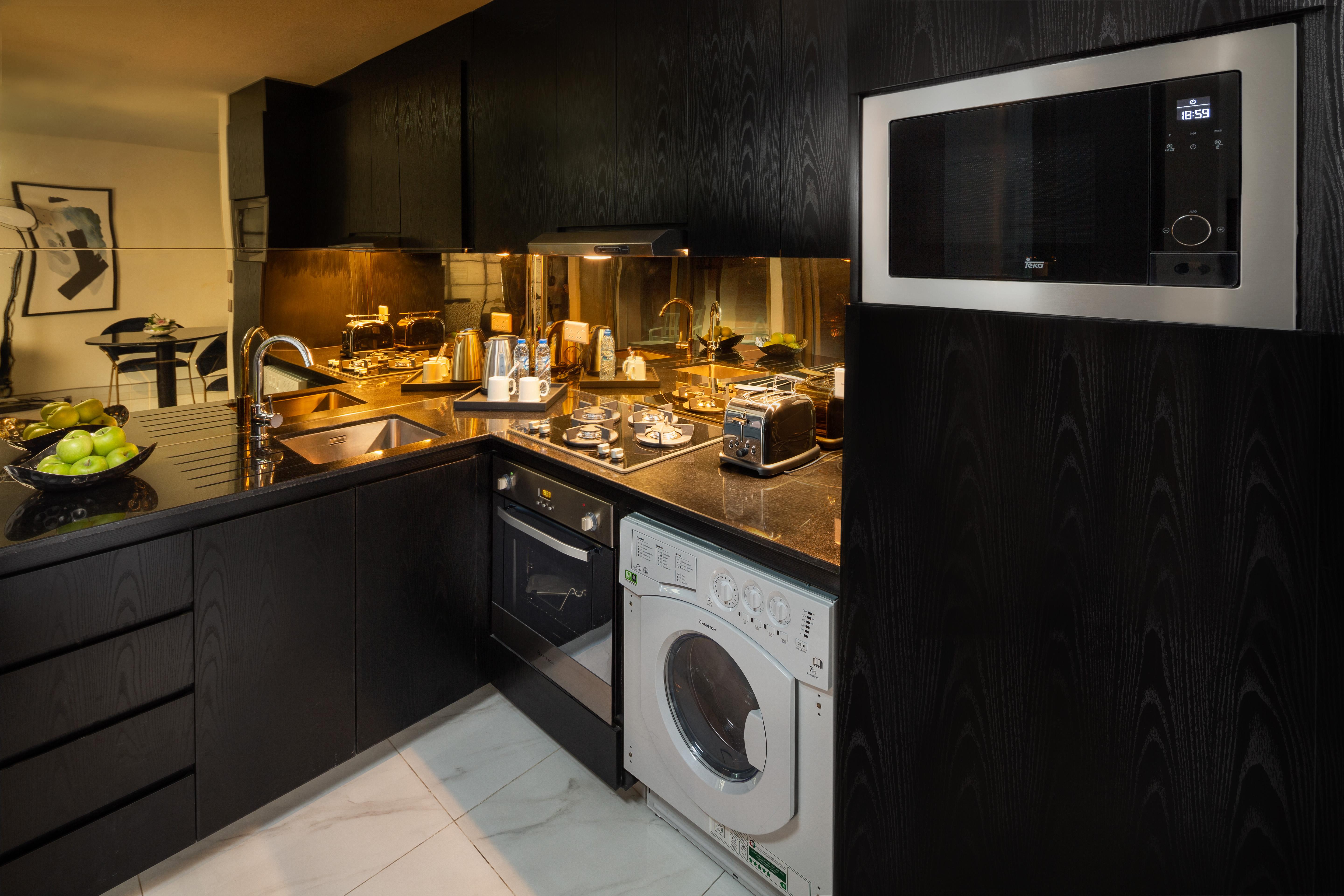 Millennium Atria Business Bay Aparthotel Dubai Ngoại thất bức ảnh The photo shows a modern kitchen with a sleek design featuring black cabinetry and countertops. There is a sink with a faucet, a stove with multiple burners, and an oven integrated into the cabinetry. A microwave is mounted above the counter for conv