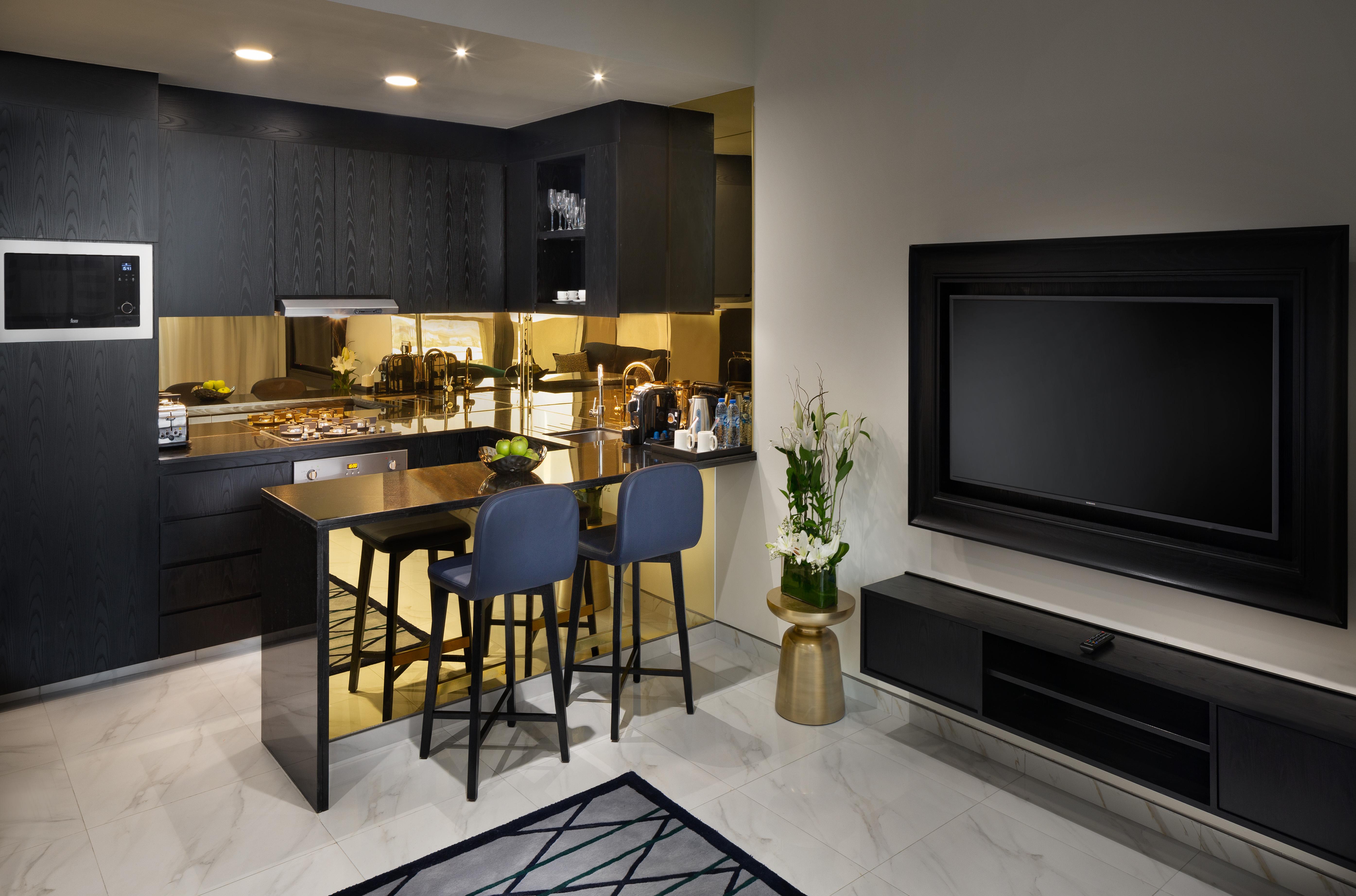 Millennium Atria Business Bay Aparthotel Dubai Ngoại thất bức ảnh The photo depicts a modern kitchen and living area. The kitchen features dark cabinetry with a clean design, showcasing various appliances, including a stovetop and possibly an oven. There is a kitchen island with two stools, suggesting a space for c