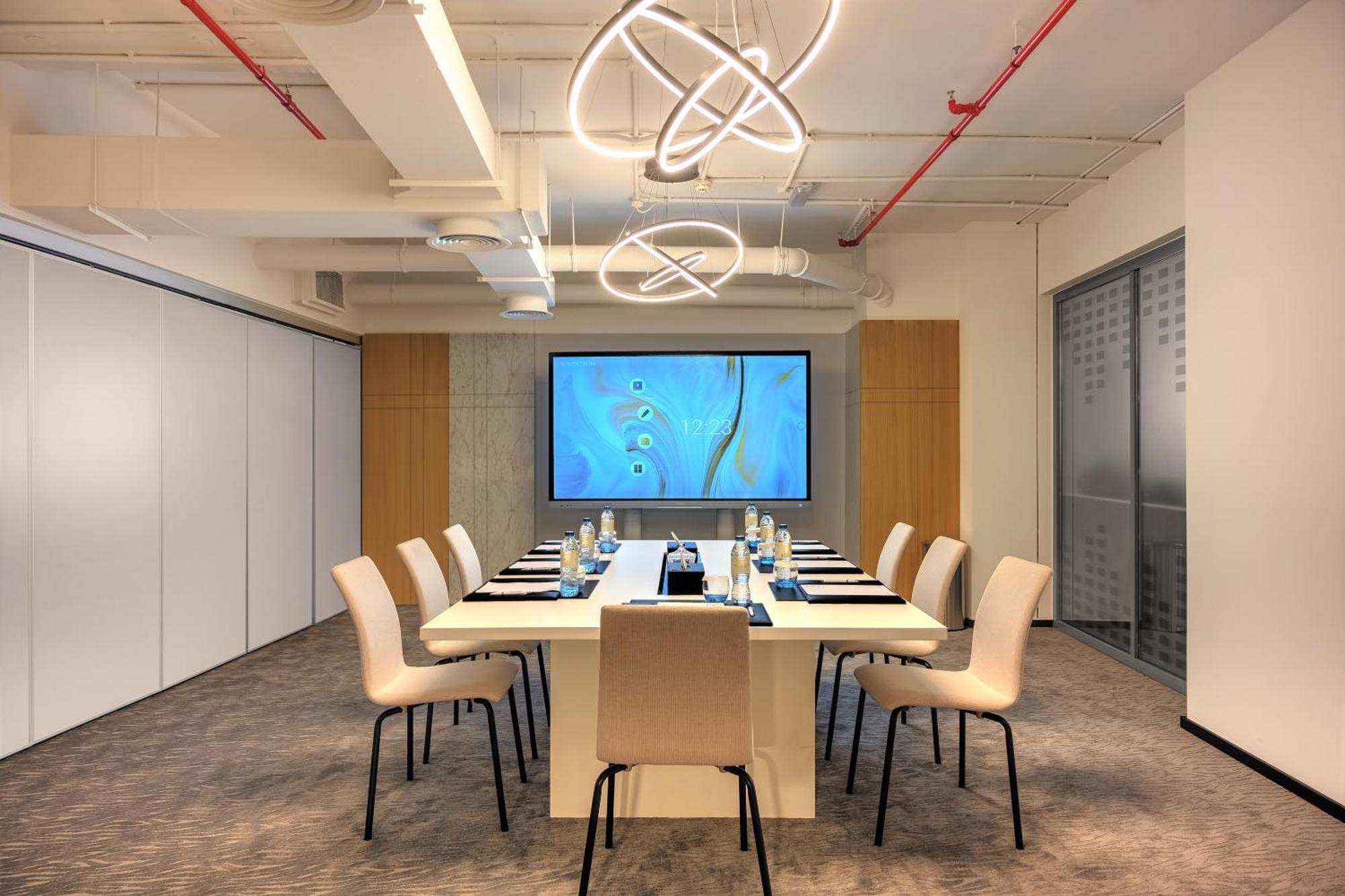 Millennium Atria Business Bay Aparthotel Dubai Ngoại thất bức ảnh The photo shows a modern conference room designed for meetings. It features a long white table surrounded by beige chairs. At the end of the table, there is a large screen displaying a blue abstract design. The room is well-lit with contemporary ligh