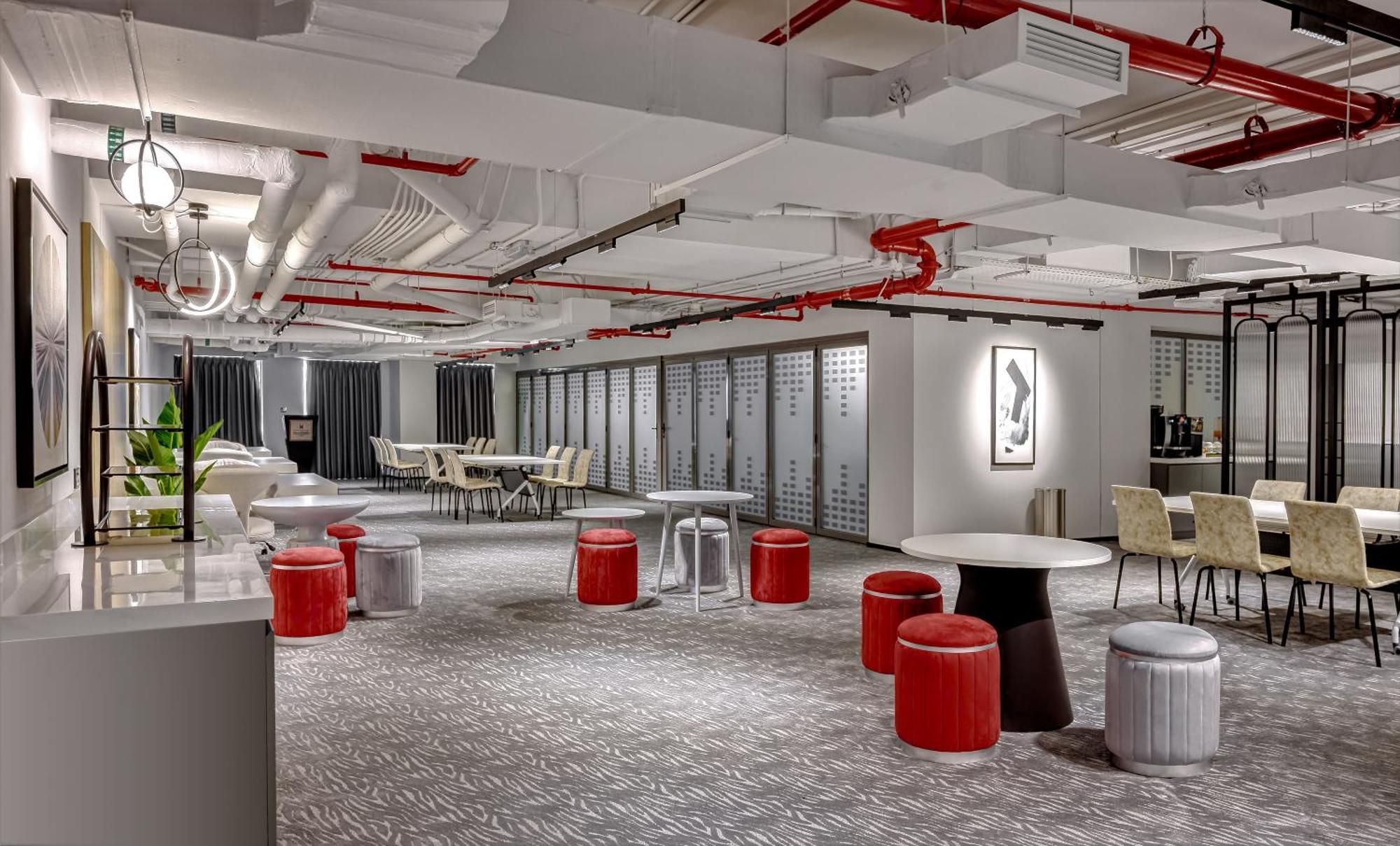 Millennium Atria Business Bay Aparthotel Dubai Ngoại thất bức ảnh The photo shows a modern interior space, likely an office or communal area. The flooring is covered with a textured carpet, and the ceiling features exposed pipes painted red. 

There are several seating options, including small round tables with sto