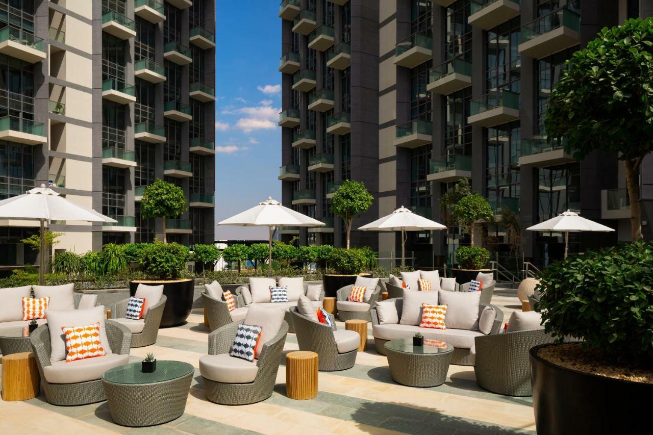 Millennium Atria Business Bay Aparthotel Dubai Ngoại thất bức ảnh The photo shows a modern outdoor lounge area, featuring several comfortable seating arrangements made of soft, stylish lounge chairs and round tables. The seating is adorned with colorful pillows, adding a pop of color to the neutral tones of the fur