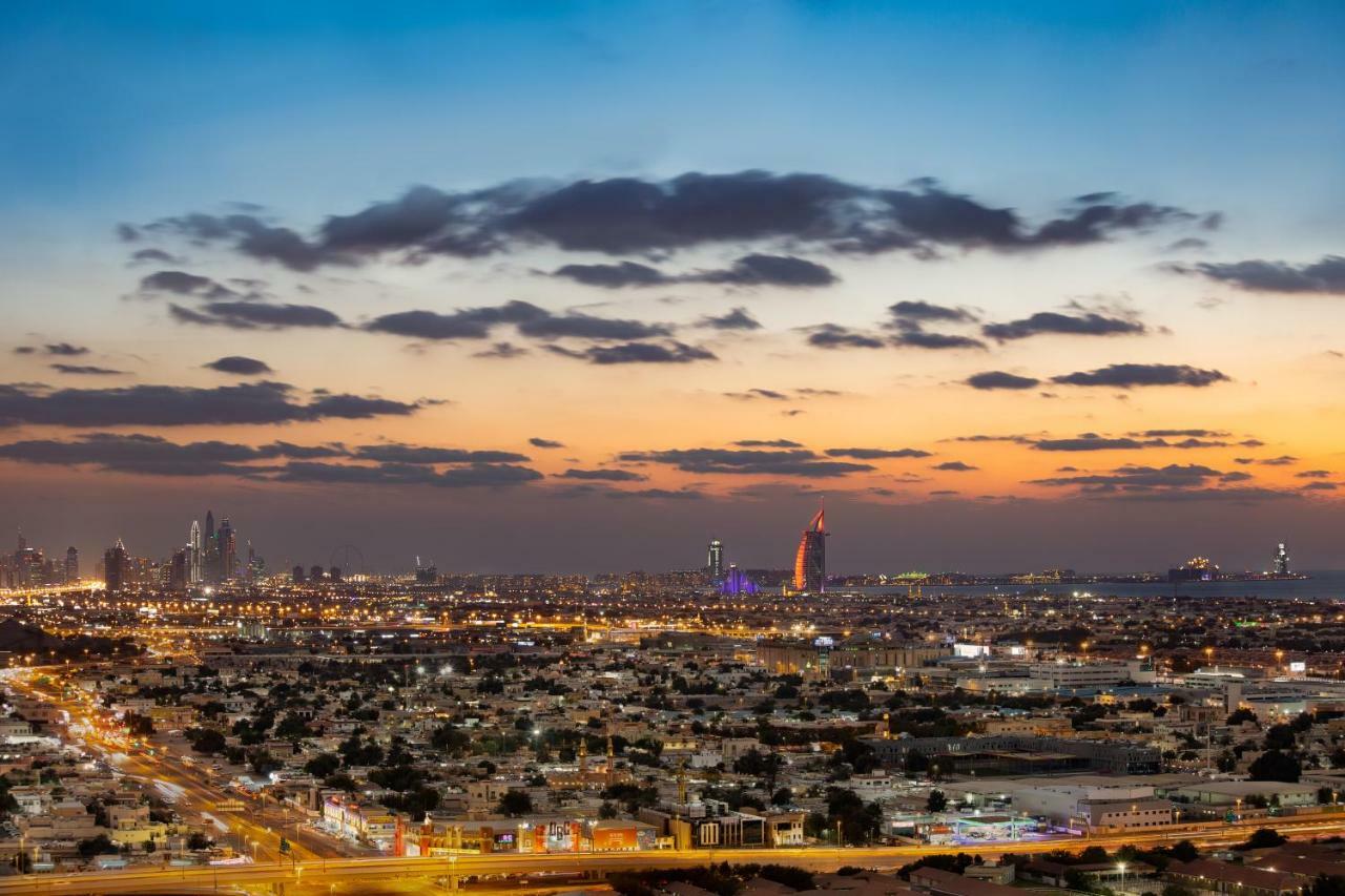 Millennium Atria Business Bay Aparthotel Dubai Ngoại thất bức ảnh The photo shows a stunning cityscape at dusk, with a panoramic view of a city skyline. The sky is transitioning from blue to orange, indicating sunset, with scattered clouds creating a colorful backdrop. In the foreground, you can see a sprawling urb